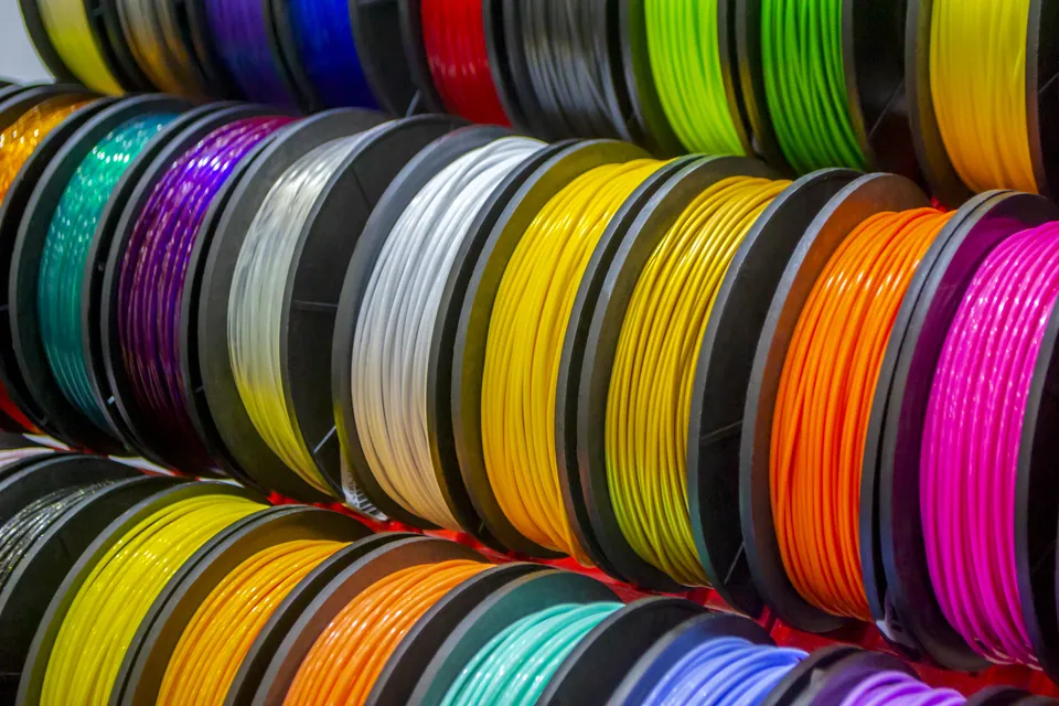 Rows of filament spools side by side on a shelf, in many bright colours from purple and silver to yellow, orange and pink.