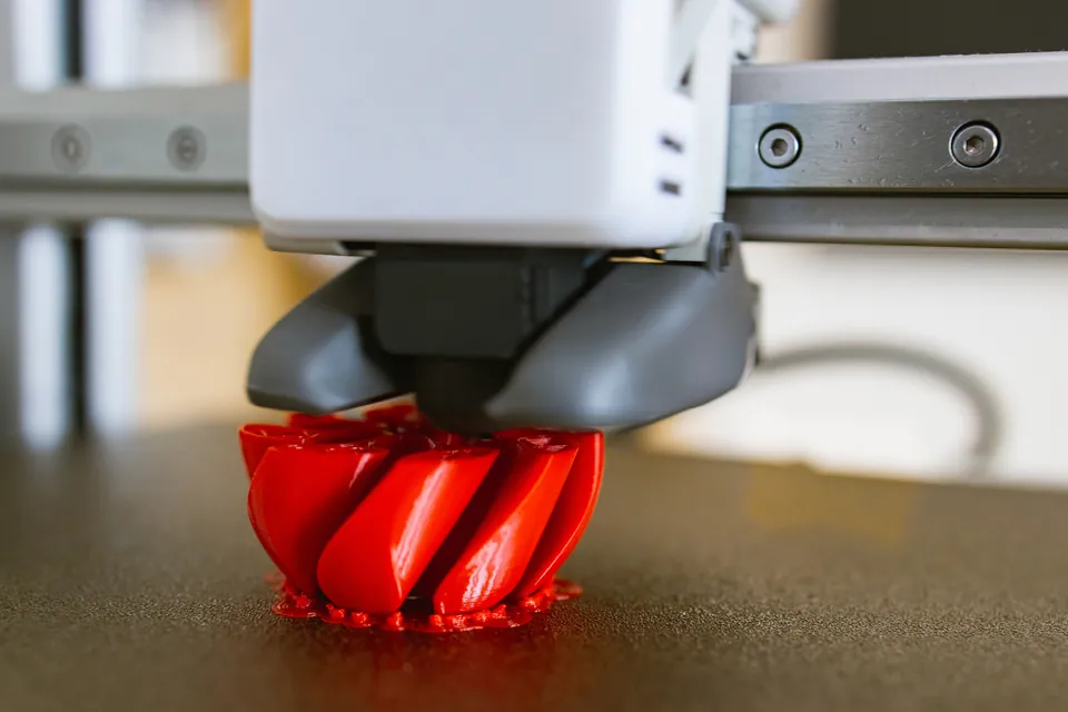Close-up of a printer nozzle building a red twisted object layer by layer on the print bed.