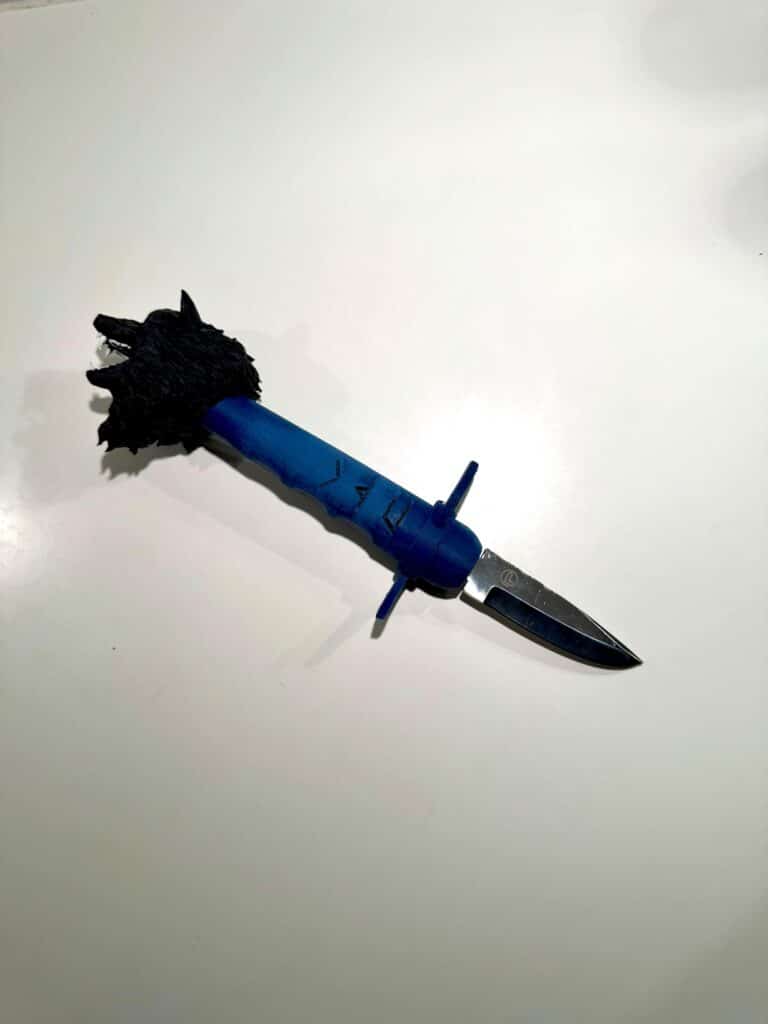 A blue-handled knife with a black wolf-shaped pommel is placed on a clean white surface, with the blade partly extended.
