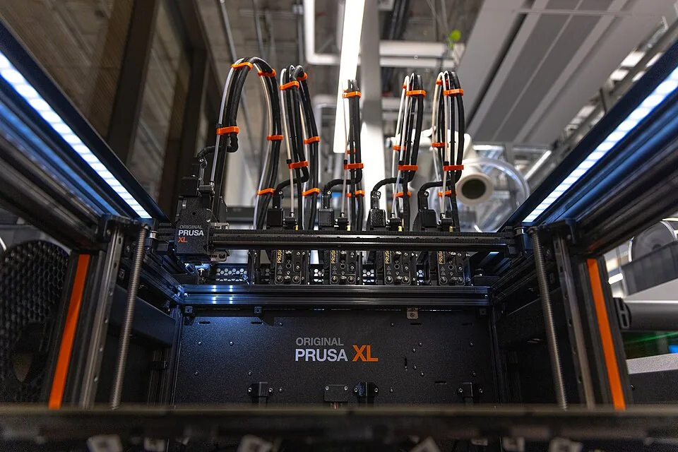 Kig ind i Prusa XL forfra, op mod docken: fem printhoveder på række under et tæt bundt af sorte og hvide rør og kabler holdt sammen med orange clips, inde i en snæver metalramme.
