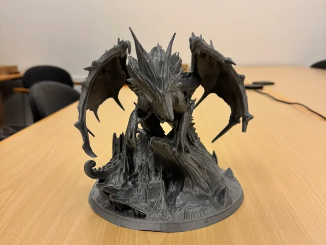 The dragon sits on a round mountain base. Its body curves around the rock, with a long tail, folded or raised wings, pointed spikes and a detailed head. The surface is busy and textured, so it is more of a display print than a simple functional object.