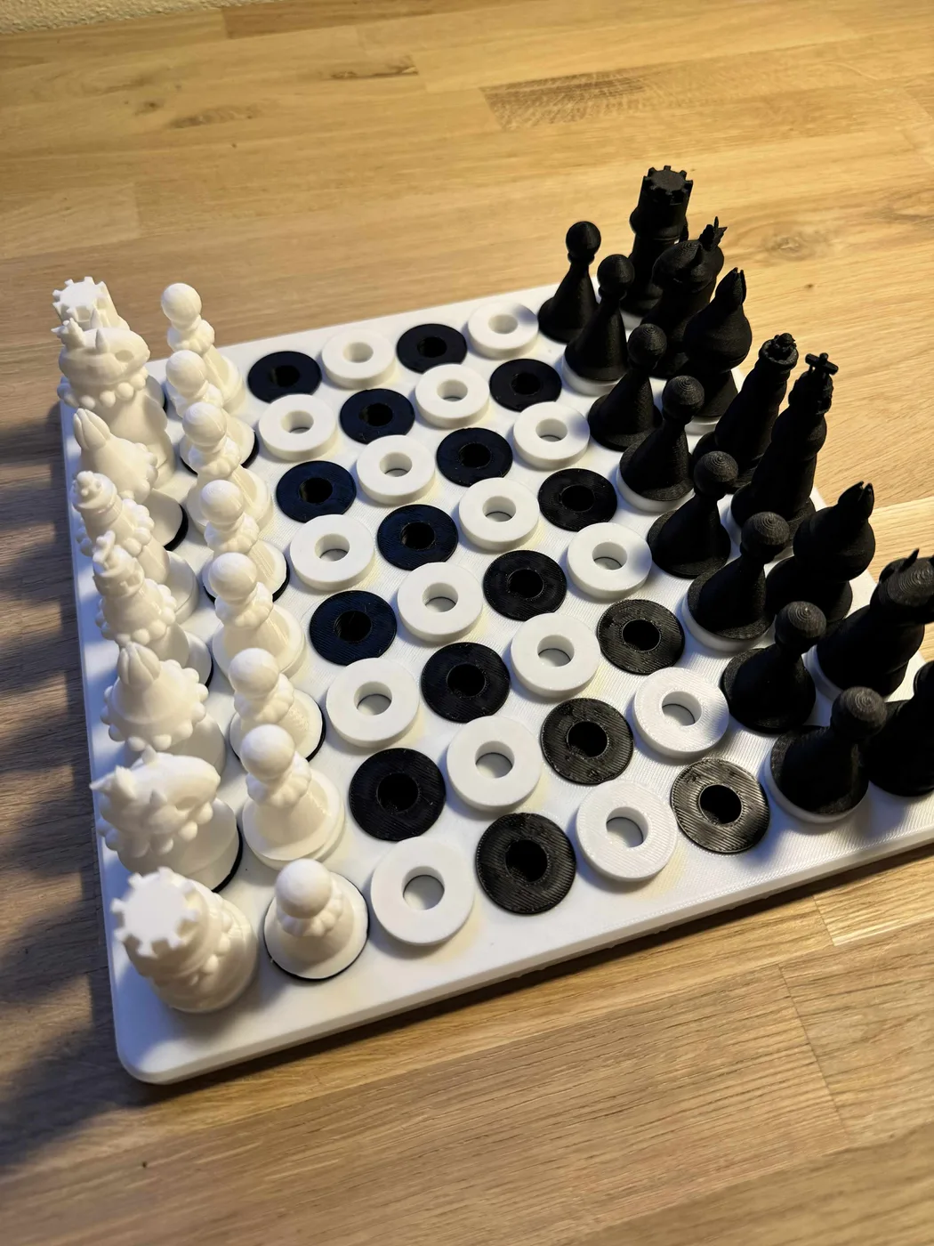 An accessible 3D-printed chess set is arranged in starting position on a tactile peg-in-hole board, with white pieces marked by raised sphere rings and smooth black pieces for touch distinction.