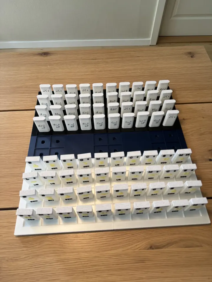 An accessible 3D-printed tactile Stratego board game is laid out in starting position, with high-contrast Braille pieces and raised rank icons.