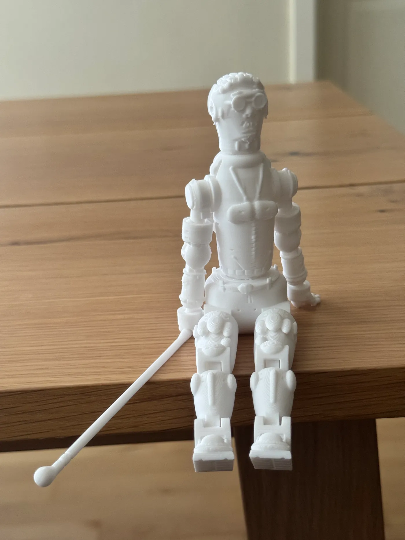Front view of the standing 3D printed blind action figure with sunglasses, arms at his sides, and the white cane angled from his right fist down to the floor in a walking stance.