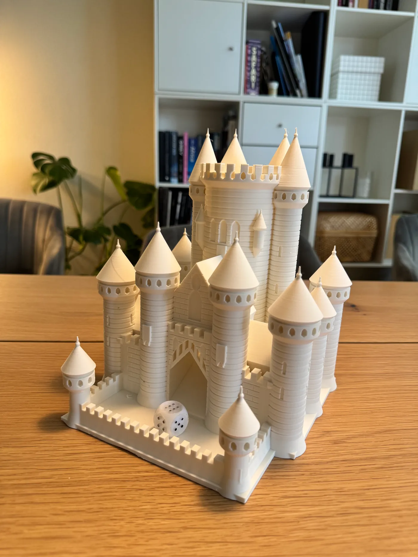 Front three-quarter photo of the white 3D printed castle dice tower standing on a wooden table, with a white die lying in the battlemented forecourt dice tray.