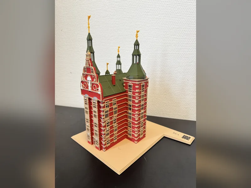 Foto af min taktile model af Rosenborg Slot set forfra fra venstre: røde murstensvægge med sandstensbånd, grønne kobbertage, forgyldte vindfløje og en lys sokkel med punktskrift og en QR-kode på højre hjørne.